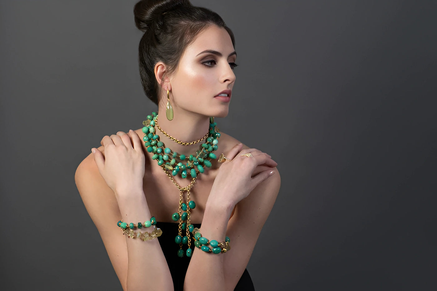 Woman wearing a green beaded necklace and bracelet against a gray background